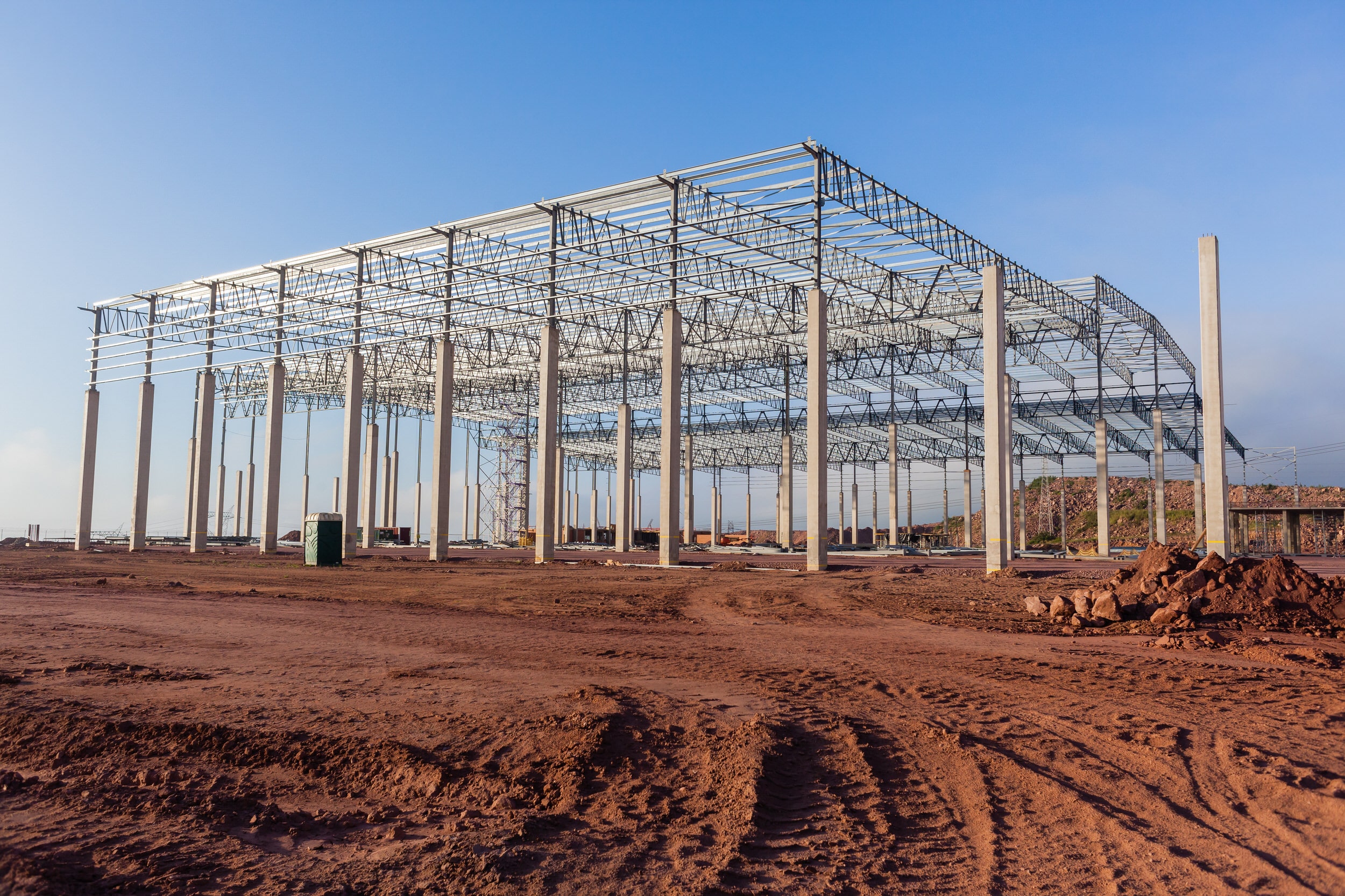 Building new large warehouse construction halfway concrete columns steel roofing beams structure landscape.